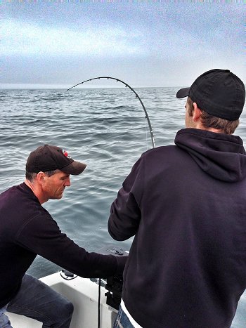 Offshore fishing is a lot of fun.  Guest with Slivers Salmon Fishing Guide John is playing a salmon on the big bank.  Water is flat and pristine. Summer fishing offshore Ucluelet offers many wonderful days